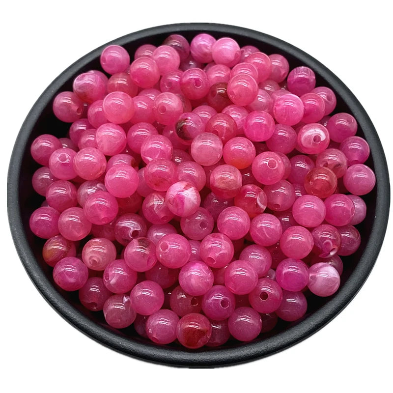 A pile of small, translucent pink and reddish round acrylic beads for jewelry making.