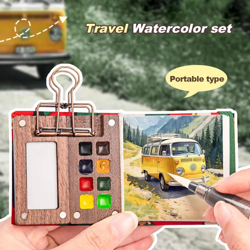 A hand holds a portable wooden watercolor paint set with various colored paints and a palette, next to a painted landscape.