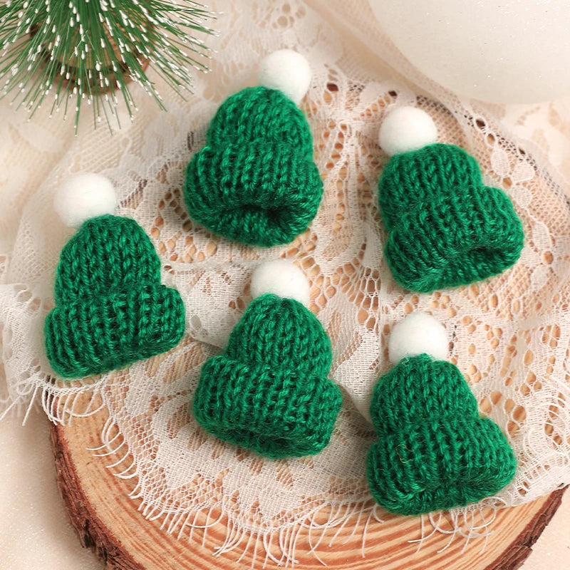 A set of mini knitted green Christmas tree hats and scarves displayed on a light fabric background.