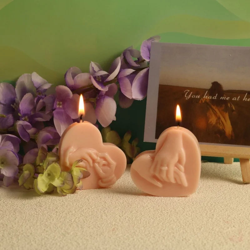 Pink heart-shaped silicone mold for candles displayed next to a framed photo and purple flowers.