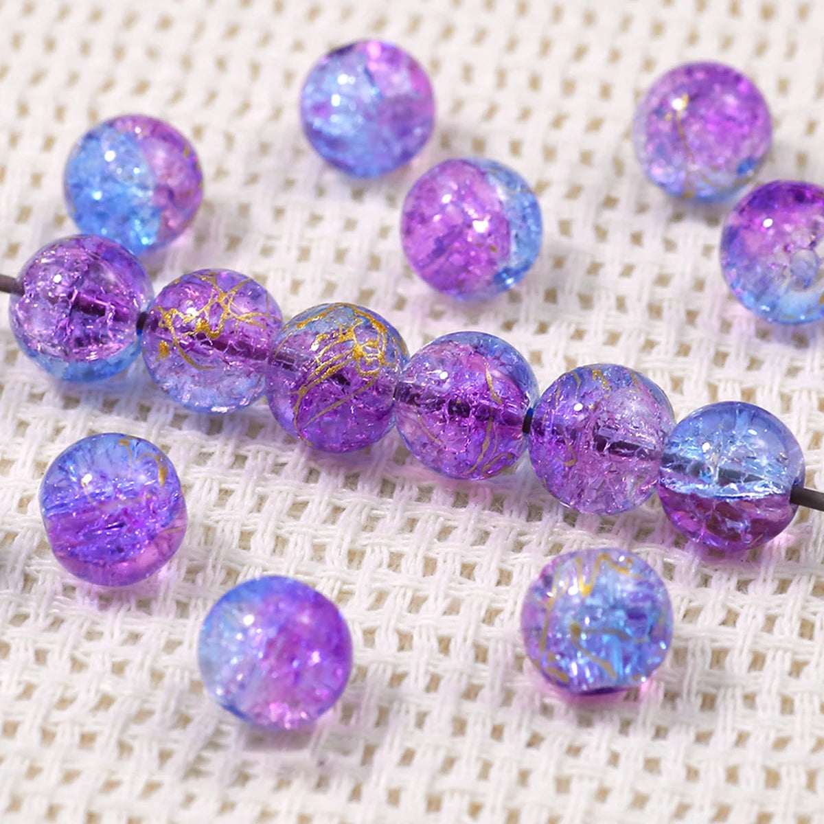Purple and blue gradient crystal glass beads with a golden crackle finish arranged on a white fabric.