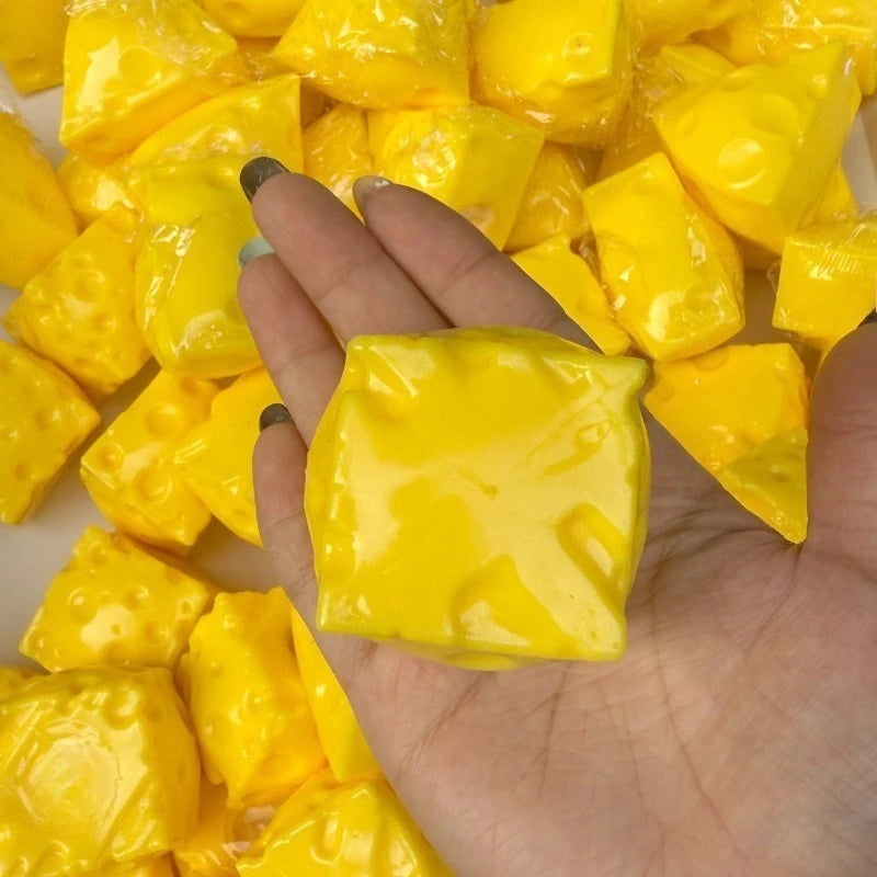 A hand holds a piece of yellow crunchy cheese ball stress relief squeeze toy surrounded by many similar pieces.