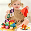 A smiling toddler holds a box of soft pulling carrot sensory toys with various colored fabric shapes.
