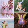 A young girl in a purple dress with glowing fairy wings is held by a boy outdoors.