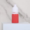 A small glass bottle of red paint with a white cap sits on a white surface.