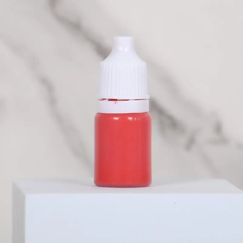 A small glass bottle of red paint with a white cap sits on a white surface.