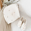 A cream quilted baby diaper caddy organizer with stroller straps resting on a light fabric surface.