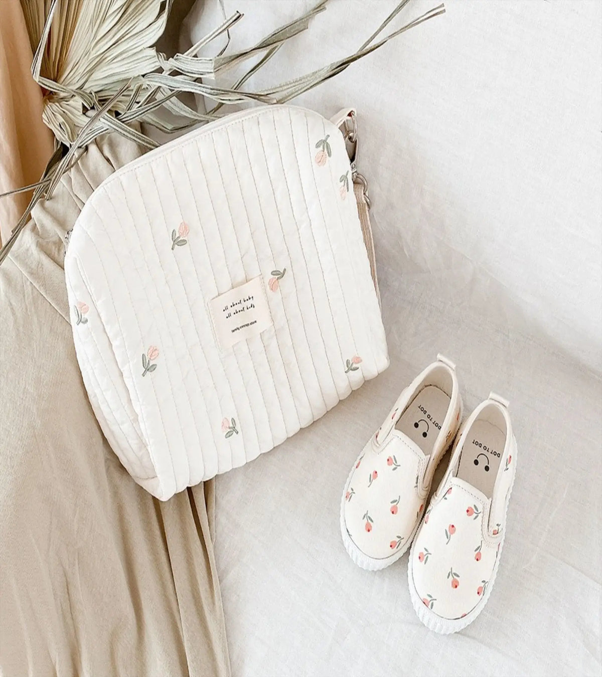 A cream quilted baby diaper caddy organizer with stroller straps resting on a light fabric surface.