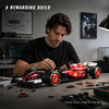 A man is assembling a detailed red 1:8 scale open-wheel racing car model kit on a dark table.