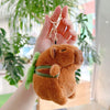 A fluffy brown capybara plush toy attached to a silver keychain charm, held in a person's hand.