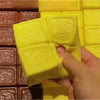 A hand is squeezing a yellow strawberry milk squishy stress relief toy, shown next to brown squishies.
