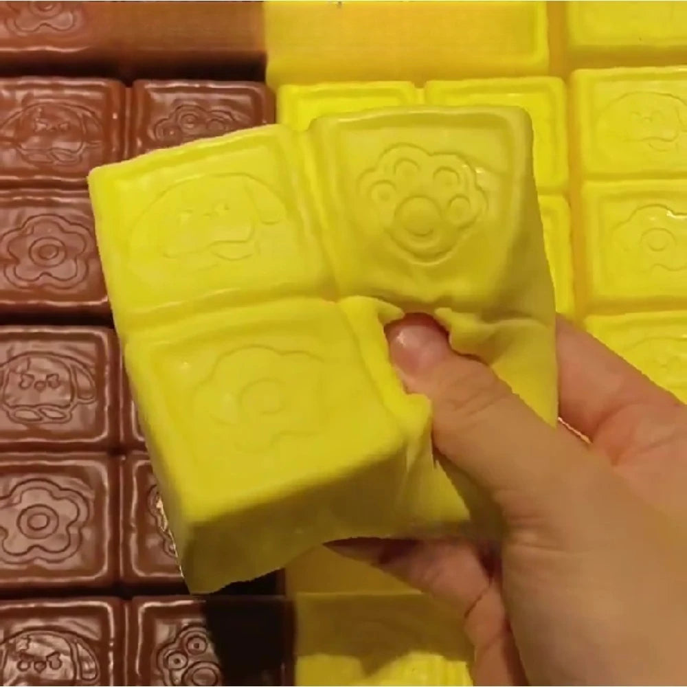 A hand is squeezing a yellow strawberry milk squishy stress relief toy, shown next to brown squishies.