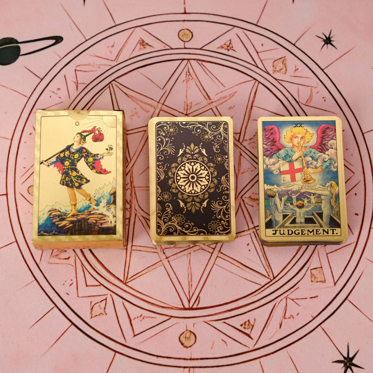 Three mini gold foil tarot cards, including the Judgment card, are arranged on a pink background with a circular geometric de
