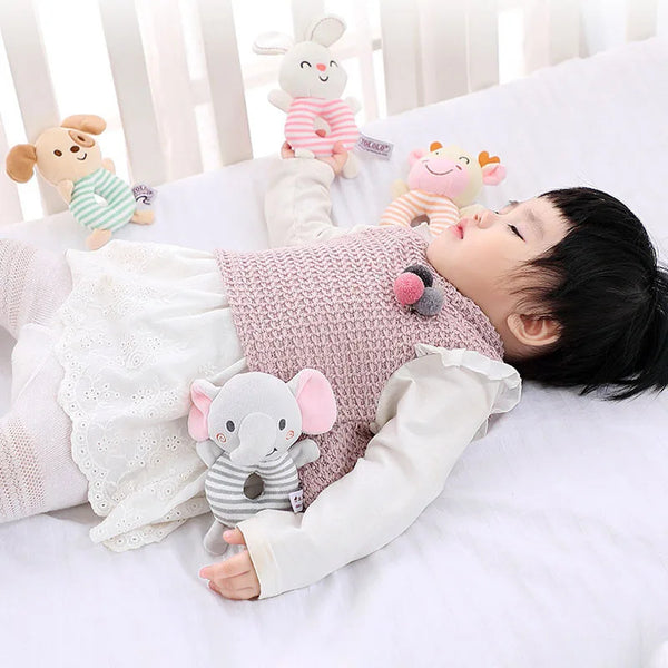 A baby is lying on a white bed surrounded by various soft cartoon animal rattle toys.