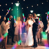 A group of people celebrating with glowing LED foam sticks in various colors under bright lights.