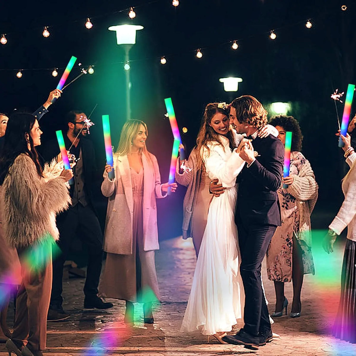 A group of people celebrating with glowing LED foam sticks in various colors under bright lights.
