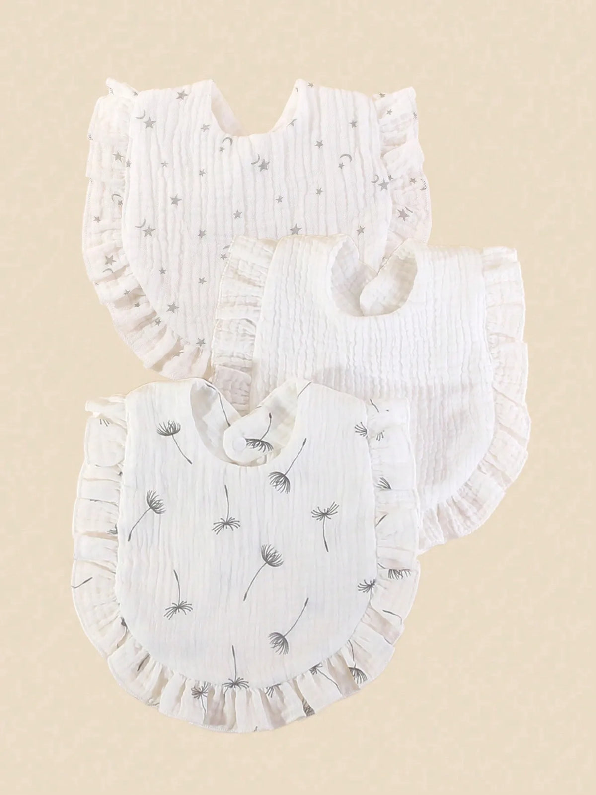 A stack of three white pure cotton muslin baby bibs with ruffled edges and embroidered stars or foliage.