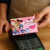 A hand holds a pink strawberry shortcake cartoon credit card sticker set featuring characters and strawberries on a black cal