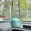 Handmade crochet chicken charm with a green head hanging from a brown string on a car interior.
