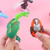 A hand holds a green dinosaur egg toy with a green head and an orange and gray body, next to a dark brown dinosaur figure.
