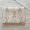 A cream muslin swaddle blanket featuring a floral print of small pink rabbits.