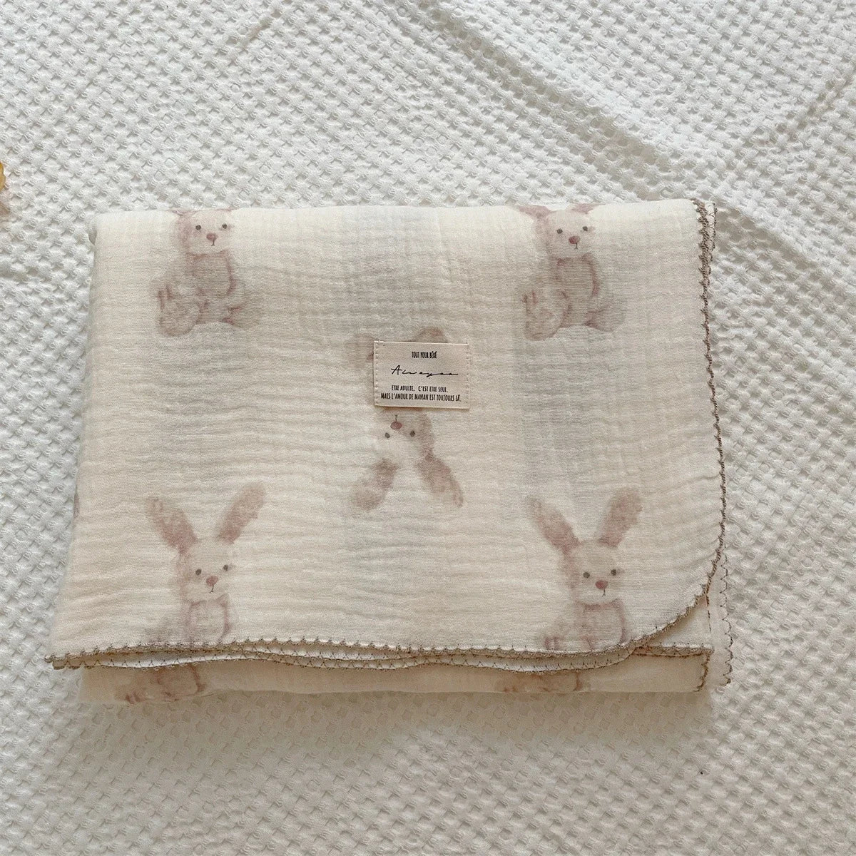 A cream muslin swaddle blanket featuring a floral print of small pink rabbits.