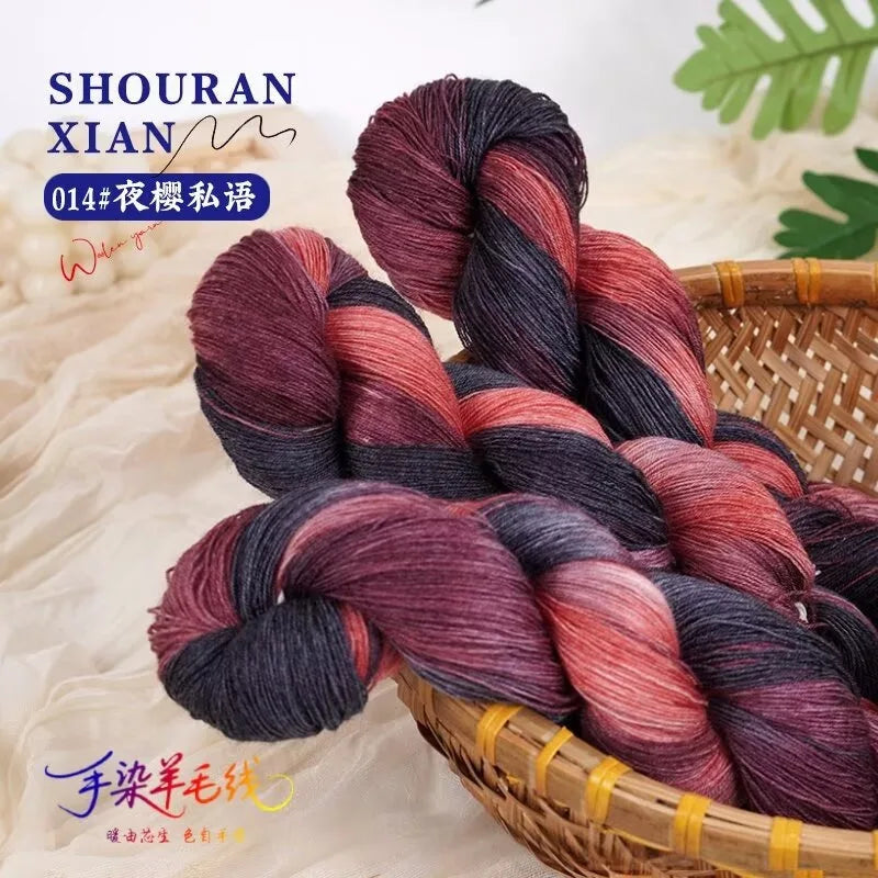 A skein of hand-dyed wool yarn featuring a gradient of pink, red, and black colors, displayed in a woven basket.