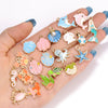 A hand displays various enamel marine life charms, including fish, sea creatures, and starfish, for jewelry making.