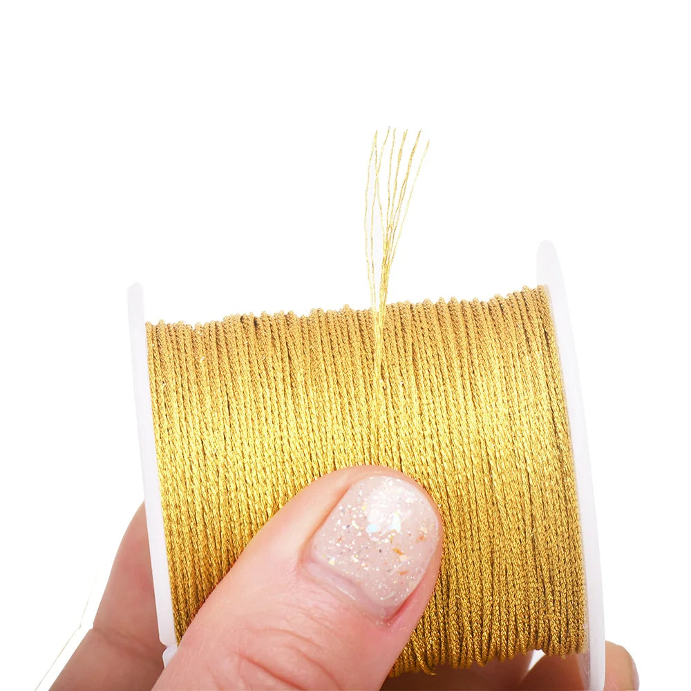 A hand holds a spool of metallic gold craft cord for jewelry making with a single strand extending from it.