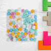 A collection of colorful sensory play sand or beads in various shades of blue, green, yellow, and purple arranged on a white 