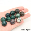 A hand holds several polished crystal spheres of India Agate, displaying various shades of green and brown.