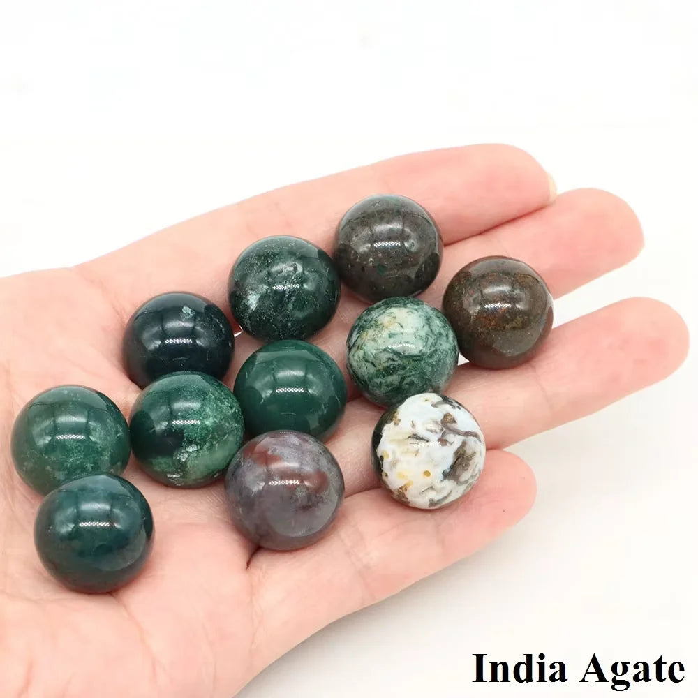 A hand holds several polished crystal spheres of India Agate, displaying various shades of green and brown.