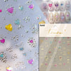 A collection of gold and iridescent nail art stickers featuring hearts, butterflies, and decorative elements on a light backg