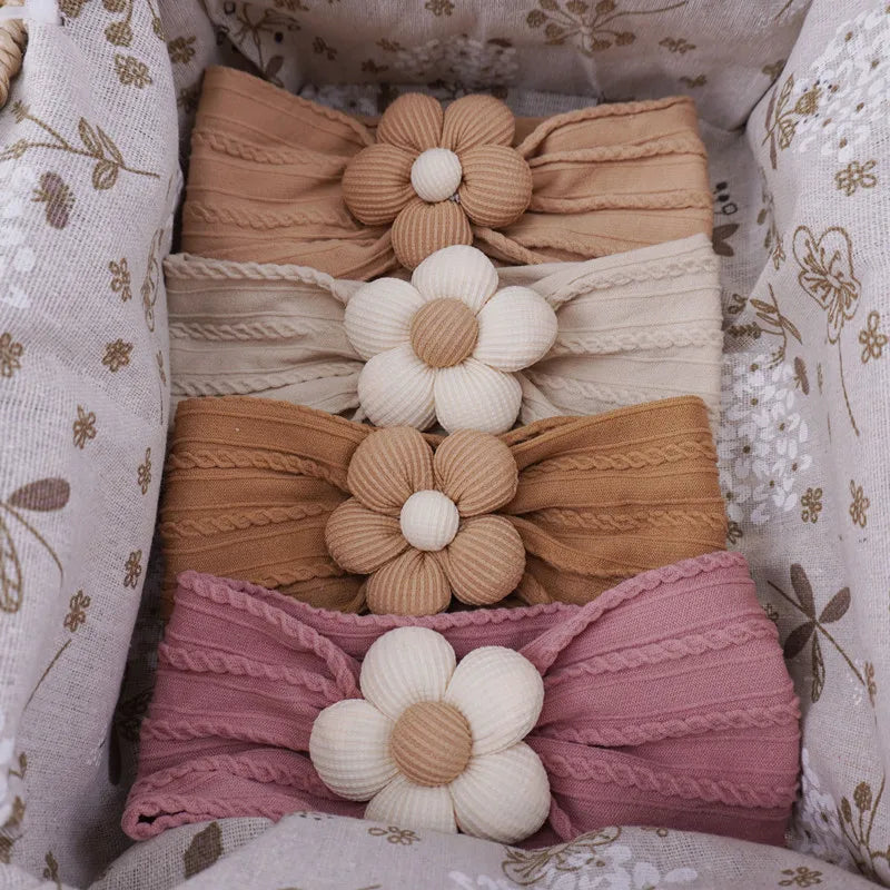 A collection of pink, beige, and mauve floral elastic baby headbands arranged in a box.