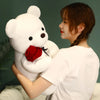A young woman is hugging a white teddy bear plush toy that has a red rose attached to its chest.