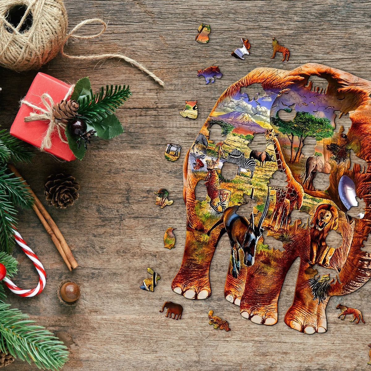 A wooden jigsaw puzzle depicting an elephant in a jungle scene is scattered on a wooden surface with festive greenery and nat