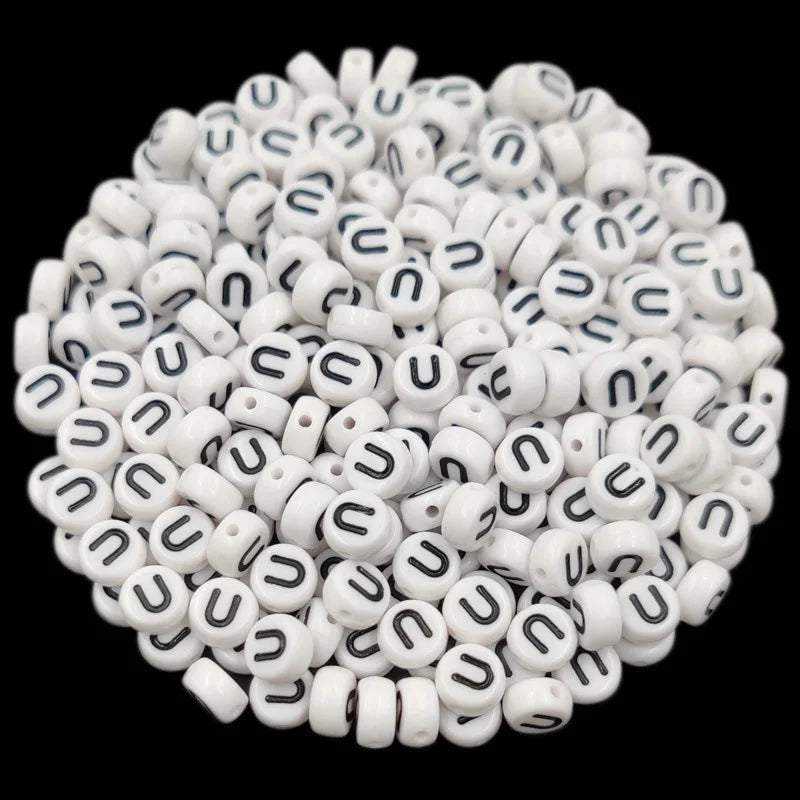 A pile of small white acrylic alphabet letter beads for jewelry making