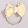 A pale yellow fabric bow headband with a beige elastic band, suitable for a baby or girl.
