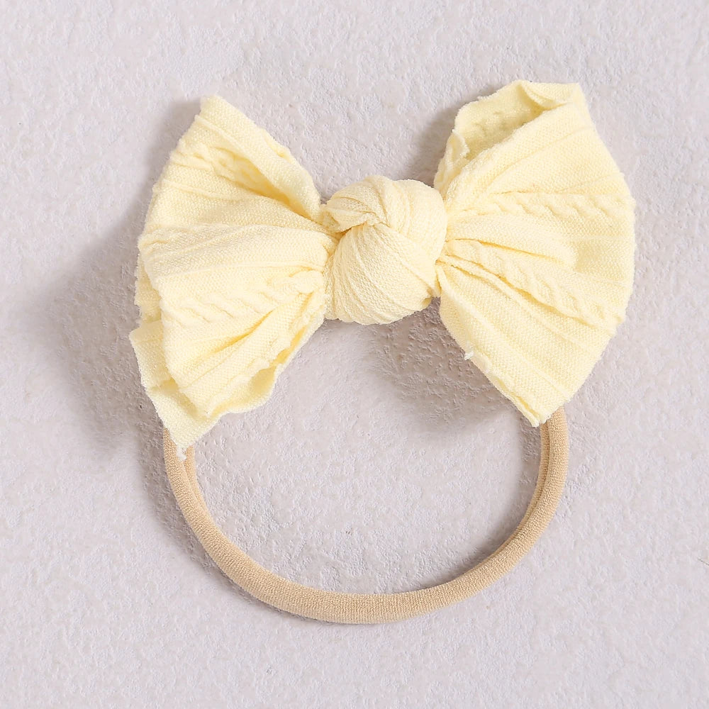 A pale yellow fabric bow headband with a beige elastic band, suitable for a baby or girl.