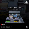 A 1:64 scale diorama depicting a street bakery scene with several diecast cars.