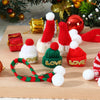A set of mini knit Christmas hats and scarves in red, green, and white yarn displayed on a wooden board.