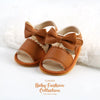 A pair of tan leather baby summer sandals with bowknot details shown on a white background.