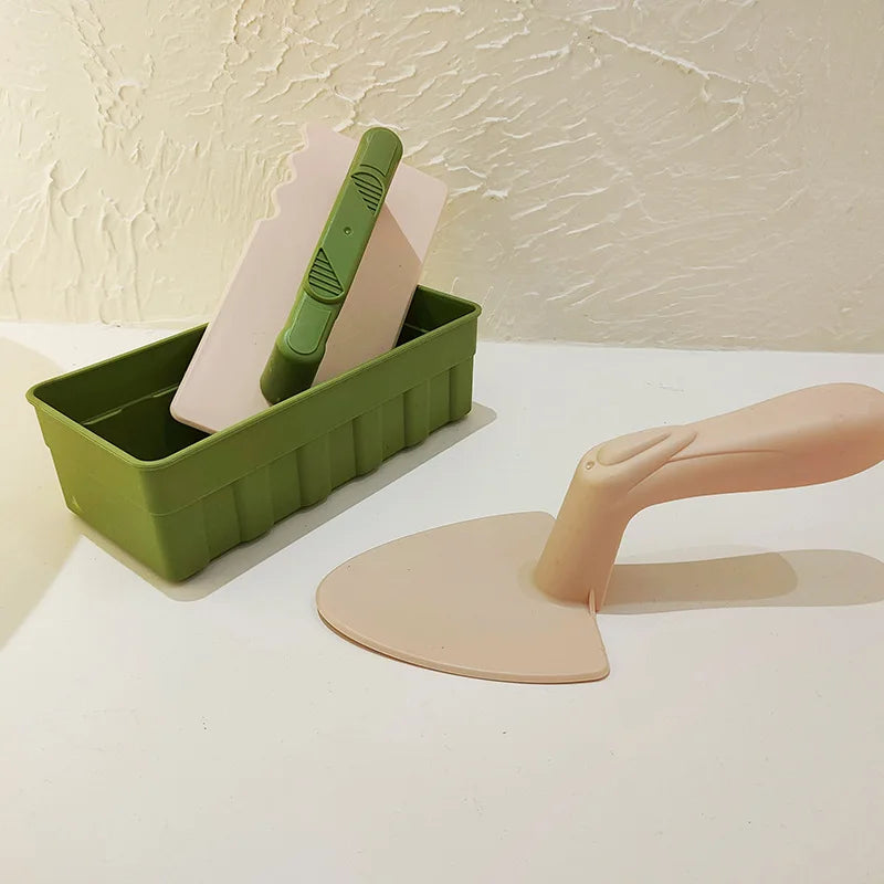 A green plastic tray holds pink and green molds for building sand and snow structures, including a shovel mold.