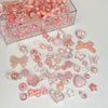 A clear box filled with pink and clear acrylic bow and flower beads for jewelry making.