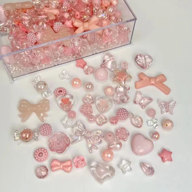 A clear box filled with pink and clear acrylic bow and flower beads for jewelry making.