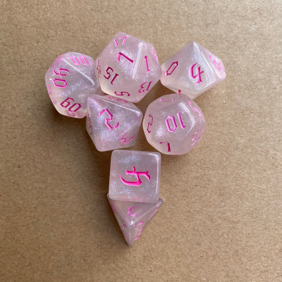 A collection of seven pink glitter polyhedral dice scattered on a brown surface.