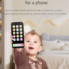 A baby is holding an interactive mobile phone toy with colorful buttons and a speaker, simulating dialing and answering.