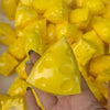 A hand holds a bright yellow, triangular cheese stress ball against a background of similar yellow pieces.