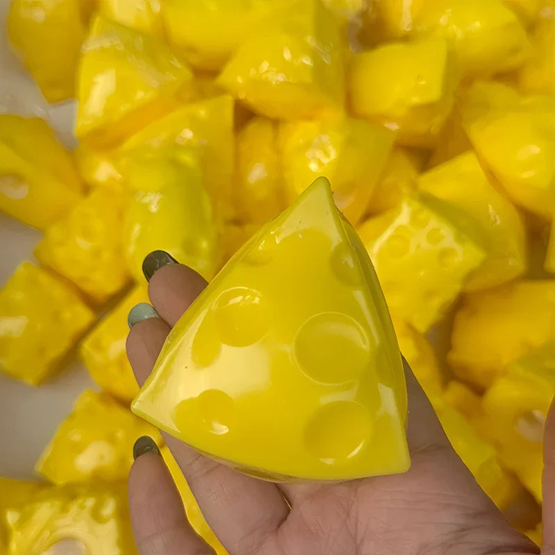 A hand holds a bright yellow, triangular cheese stress ball against a background of similar yellow pieces.