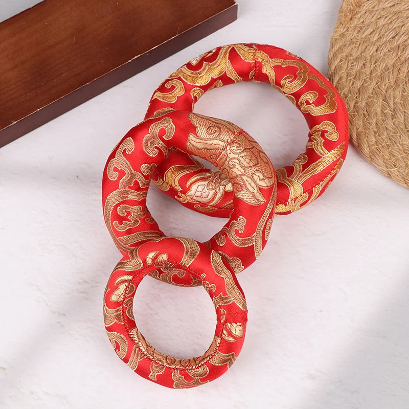 A handmade red singing bowl cushion featuring intricate gold embroidery on a fabric ring.